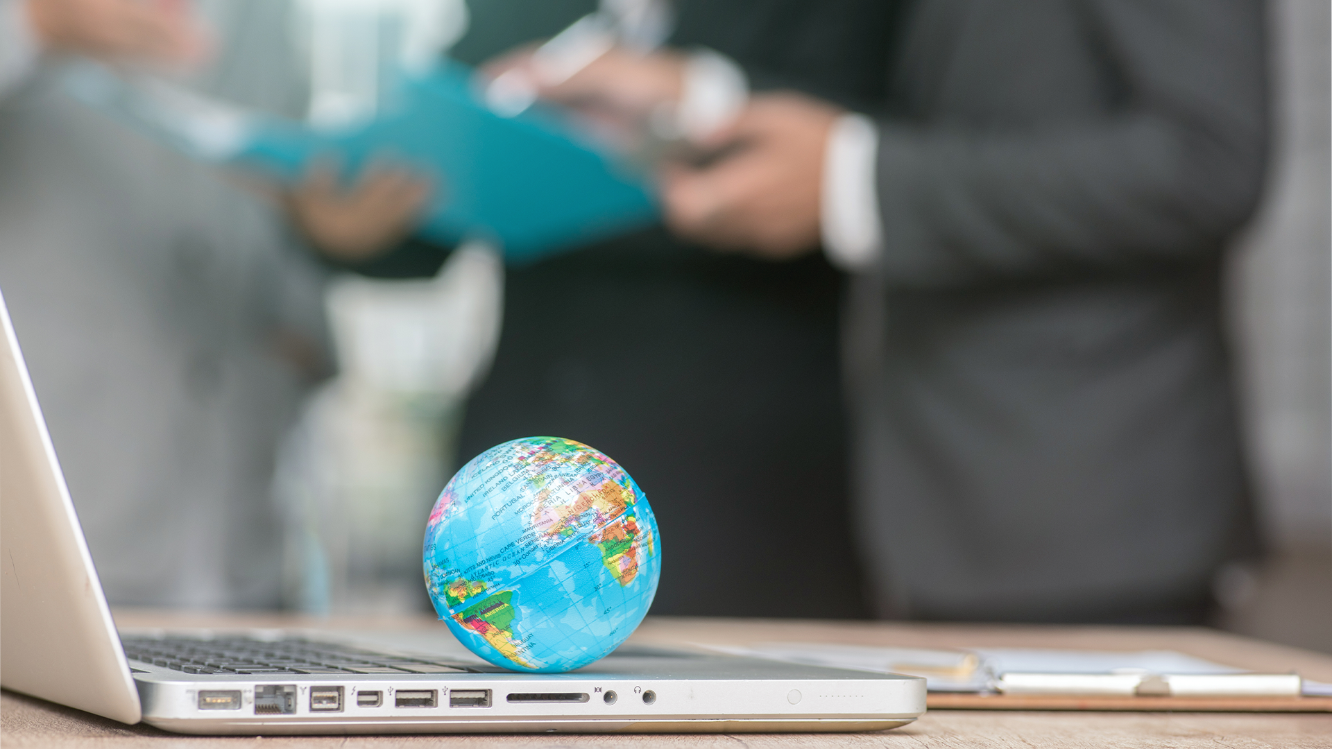 A small planet sitting on a laptop with people talking in the background